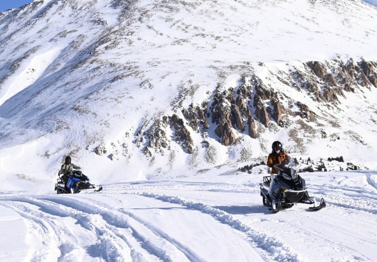 two people snowmobiling with a large mountain behind