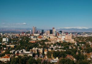 buildings and trees in the foreground with downtown Denver behind and the mountains in the background