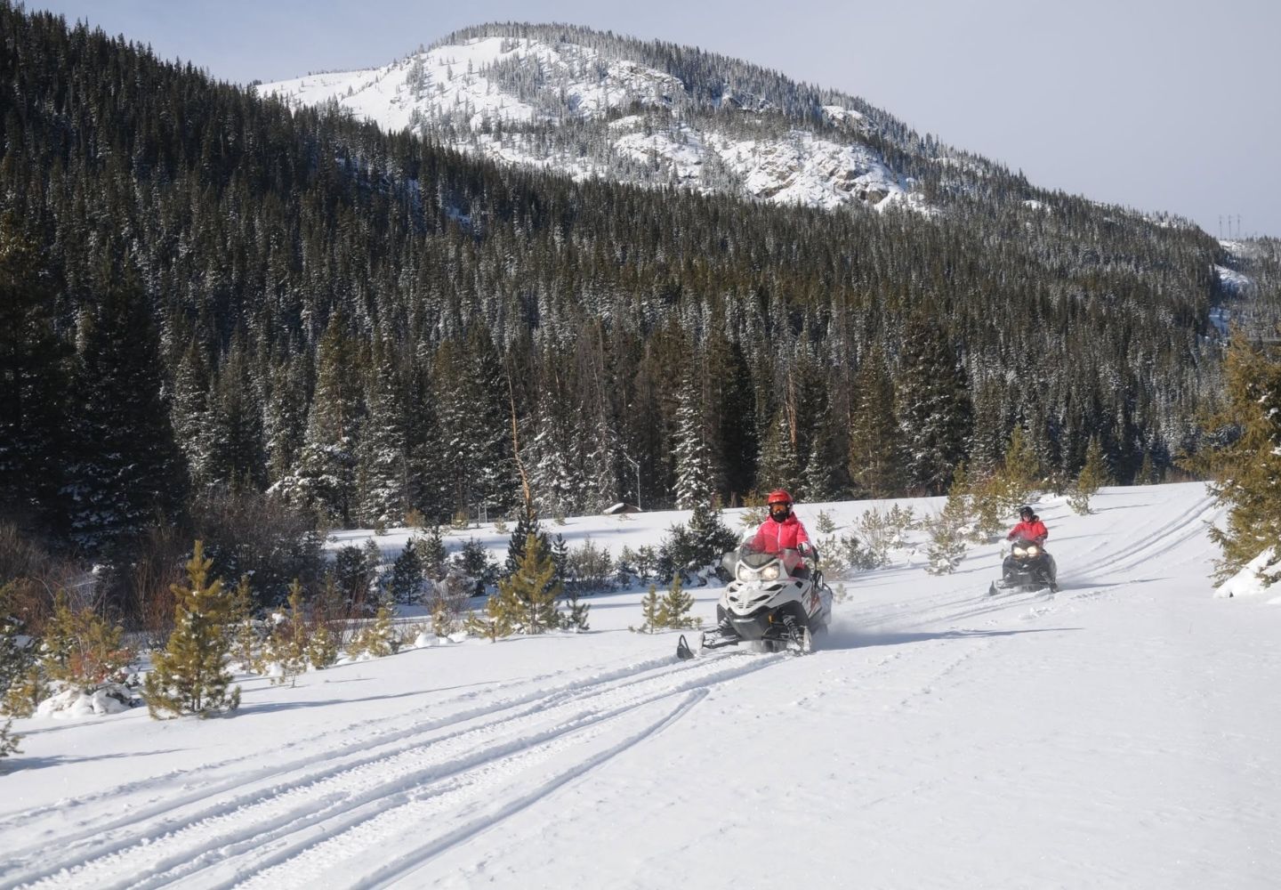 two people riding snowmobiles in the mountains