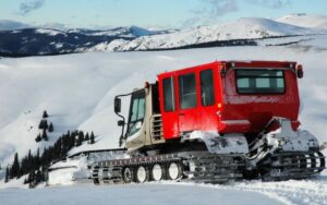 red snow groomer with mountains in the background
